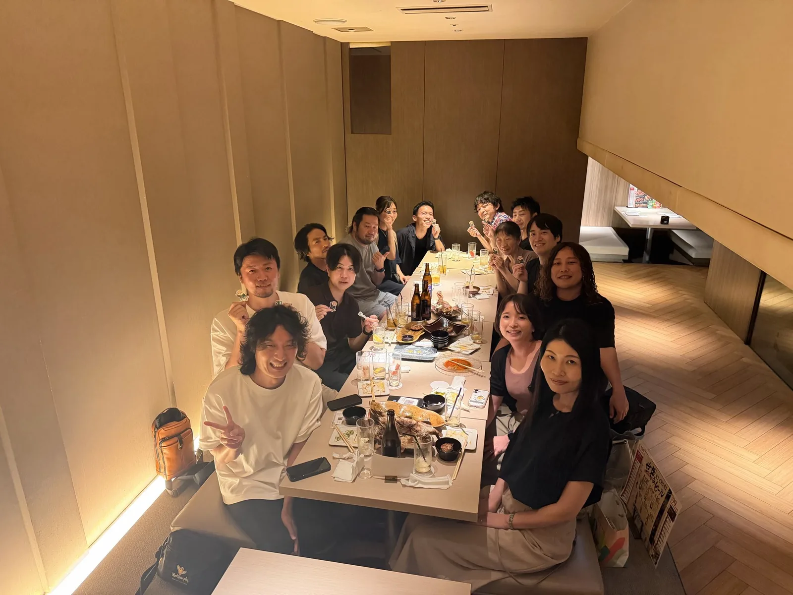居酒屋の個室で、長テーブルを囲んだ参加者がaimarkのステッカーを持って笑っている