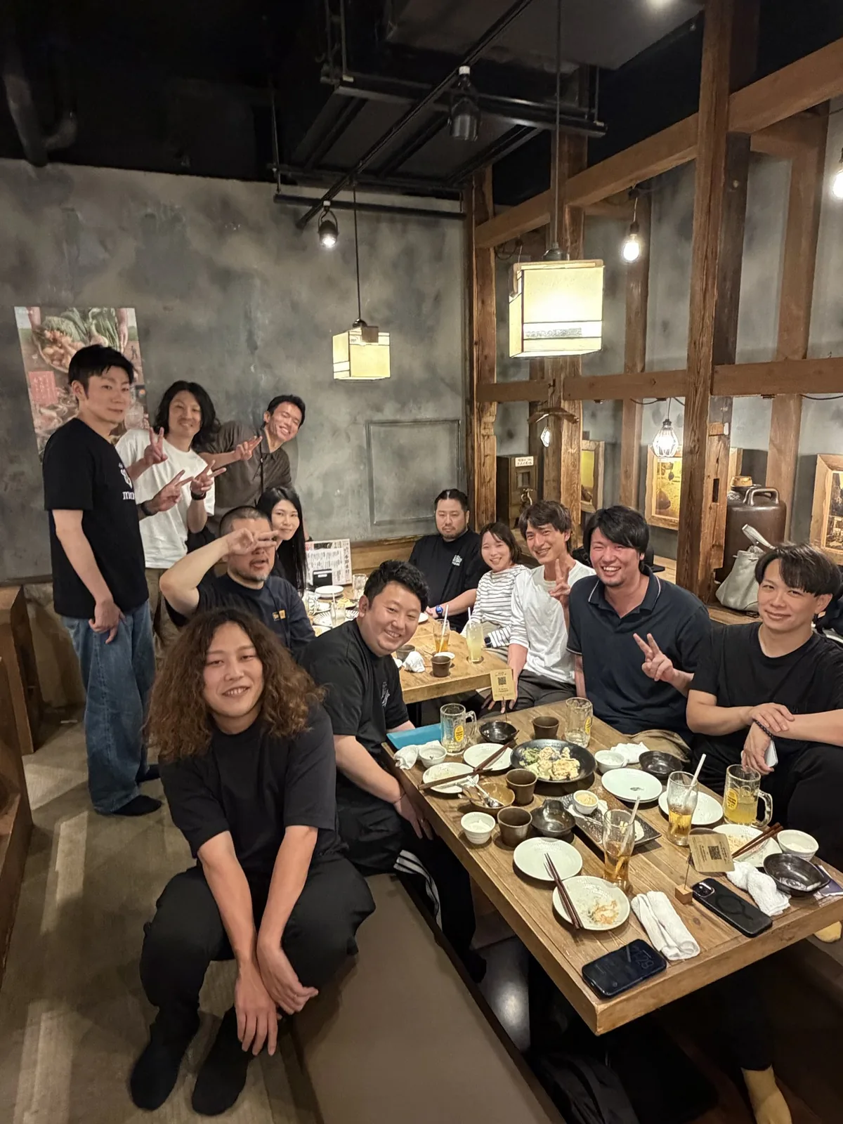 居酒屋で、立っている人も座っている人も笑顔でカメラに向かっている参加者たち