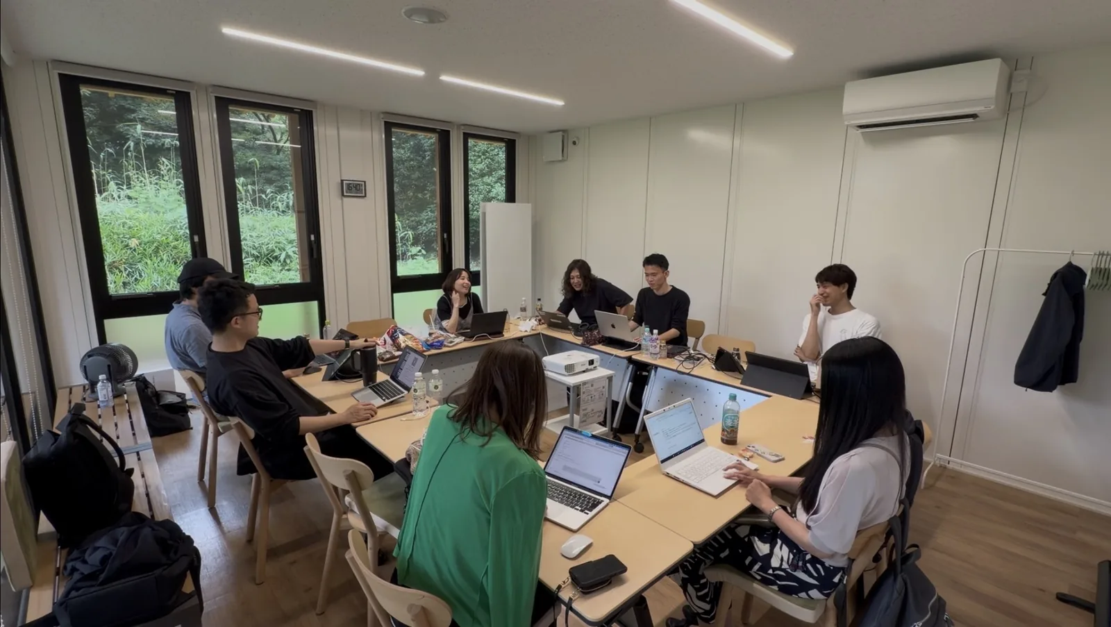 コワーキングスペースの会議室で、コの字に並んだ机にノートPCを広げて話している参加者たち